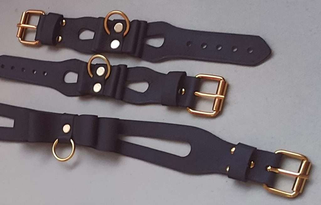 braunes Halsband und Cuffs mit Cutouts, Lederschleife, einem abnehmbaren O-Ring und einer Dornschließe nebeneinander