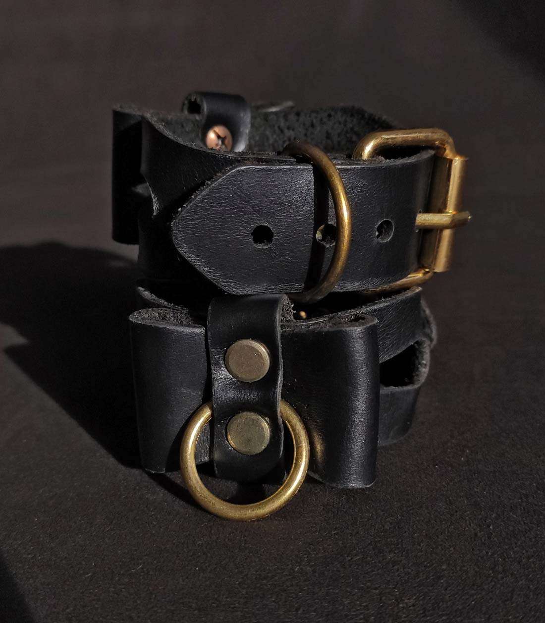 schwarze Cuffs mit Cutouts, Lederschleifen und goldener Hardware, die hinten durch eine Dornschließe verschlißbar sind
