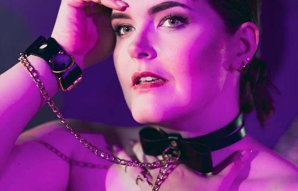 CO_BOBL_detail2 Gründerin von Make Me mit schwarzem Lederhalsband, das durch einen O-Ring und Ketten mit schwarzen Bow Cuffs verbunden ist
