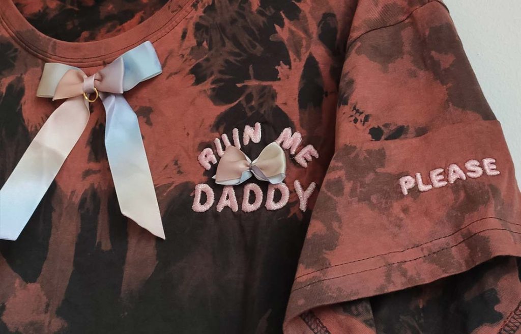 TEE_ruinme_daddy_detail T-Shirt mit Batikmuster, Schleife unterm Ausschnitt und aufgesticktem "Ruin me Daddy" sowie "Please" Schriftzug