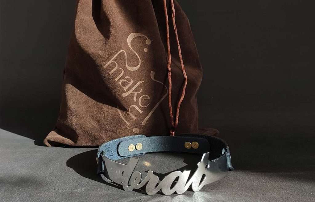 brat_co_detail schwarzes Lederhalsband mit einem Edelstahlbügel mit "brat" Schriftzug und einem Steckverschluss über Stopper mit dem passenden Stoffbeutel dazu