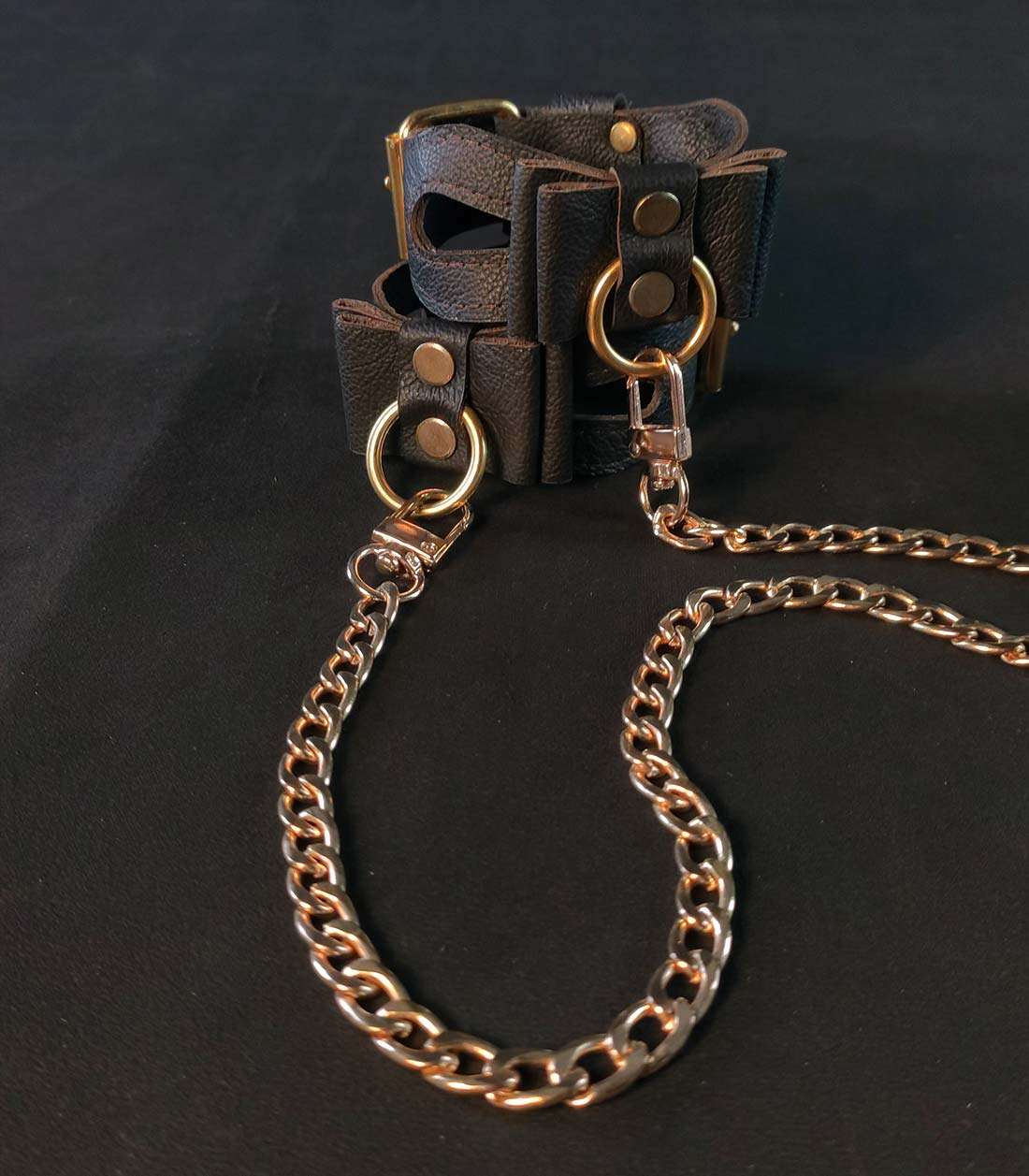 chain_con_1 braune Cuffs mit Cutouts, Lederschleifen und goldener Hardware, die mit Ketten verbunden sind