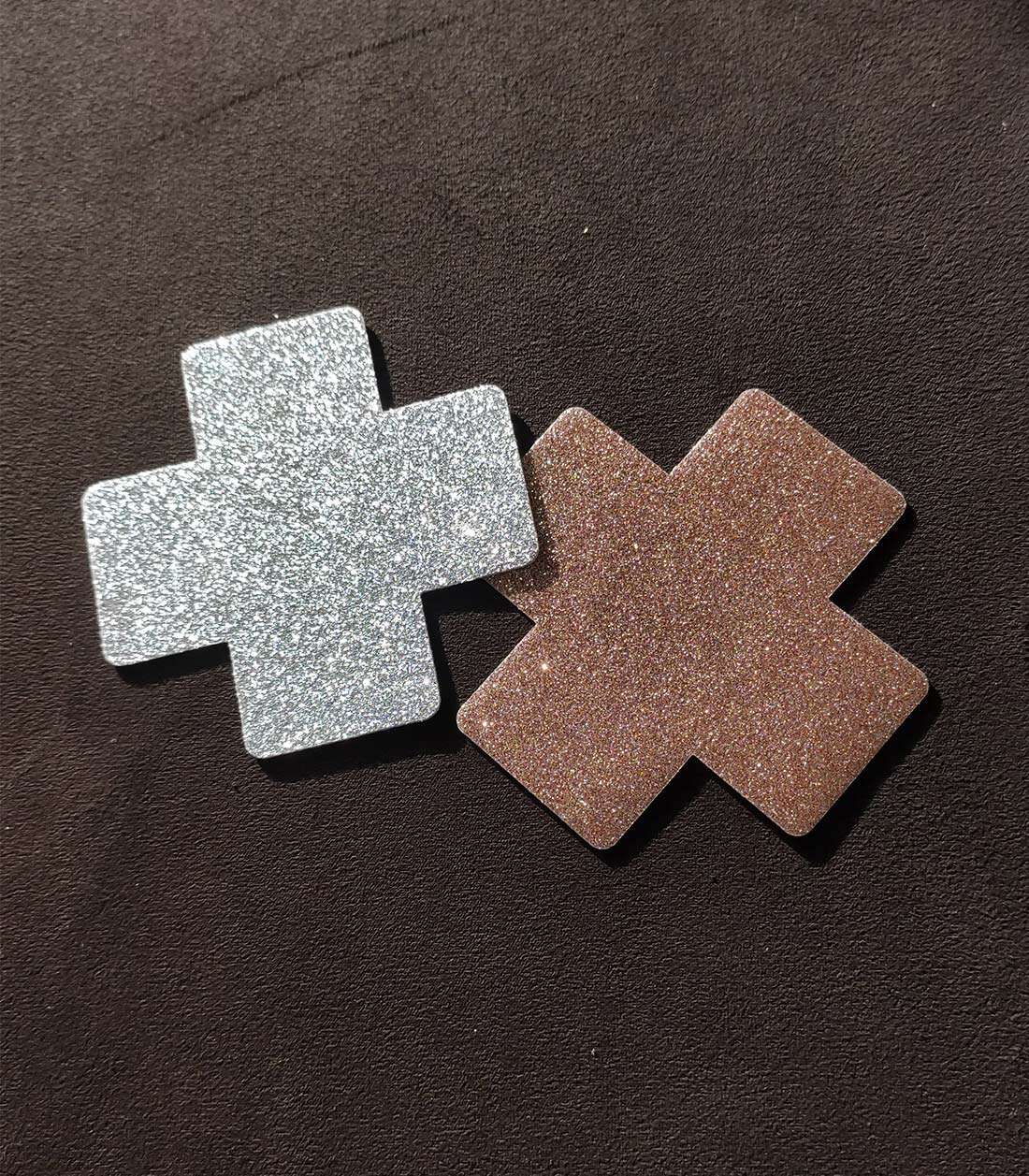 zwei glitzernde, kreuzförmige Nipple Patches in den Farben silber und rosegold liegen nebeneinander
